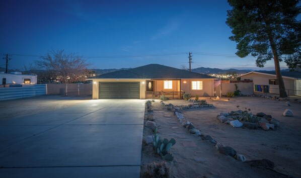 Une maison de plain-pied avec un garage, un porche à l’avant et un jardin désertique bien entretenu, agrémenté de cactus et de rochers.