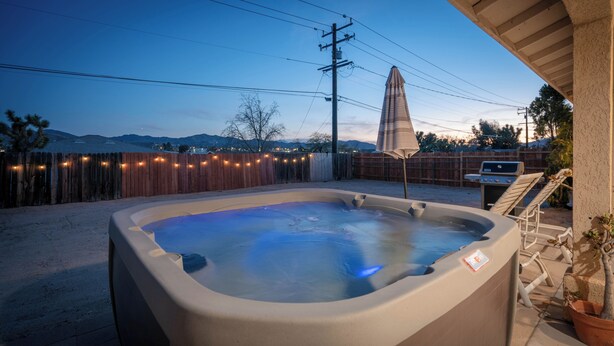 Een jacuzzi in een achtertuin met een houten omheining, een barbecue en uitzicht op bergen.
