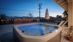 Un bain à remous dans un jardin, avec une clôture en bois, un barbecue et une vue sur les montagnes.