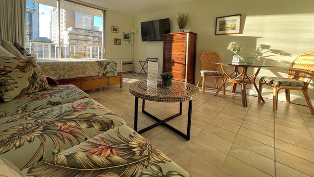 A well-lit living room with a sofa, a dining table with chairs, a cabinet, and a TV on the wall. - 🤩Great location🤩 8 guests~same floor (6)~ ✅ 2 studios ✅ free parking (Honolulu)