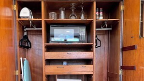 Un armario de madera con estantes, un microondas y un refrigerador pequeño.