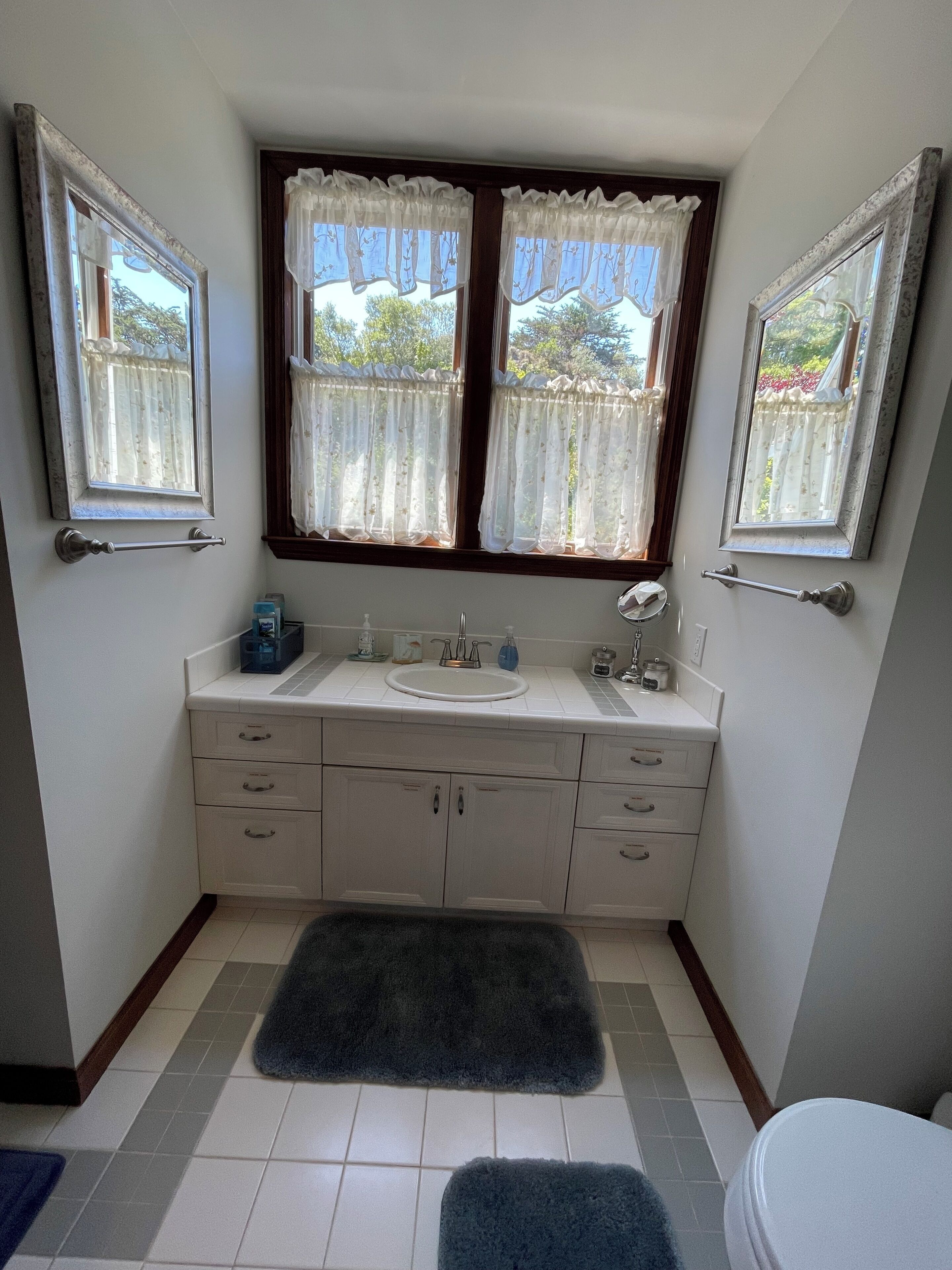 Une petite salle de bain avec deux fenêtres, un lavabo et des toilettes.