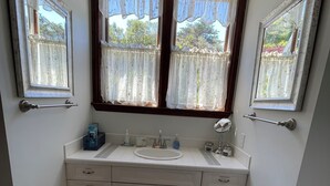 Un baño pequeño con dos ventanas, un lavamanos y un inodoro.