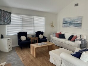 A living room with a white sofa, two armchairs, a wooden coffee table, and a large window with blinds.