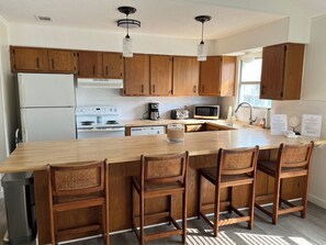 A modern kitchen with wooden cabinets, a central island with bar stools, a white refrigerator, a stove, a microwave, and a coffee maker.