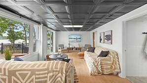 En moderne stue med et stort vindue, loft med indbygget belysning og en sofa med mønstrede puder.