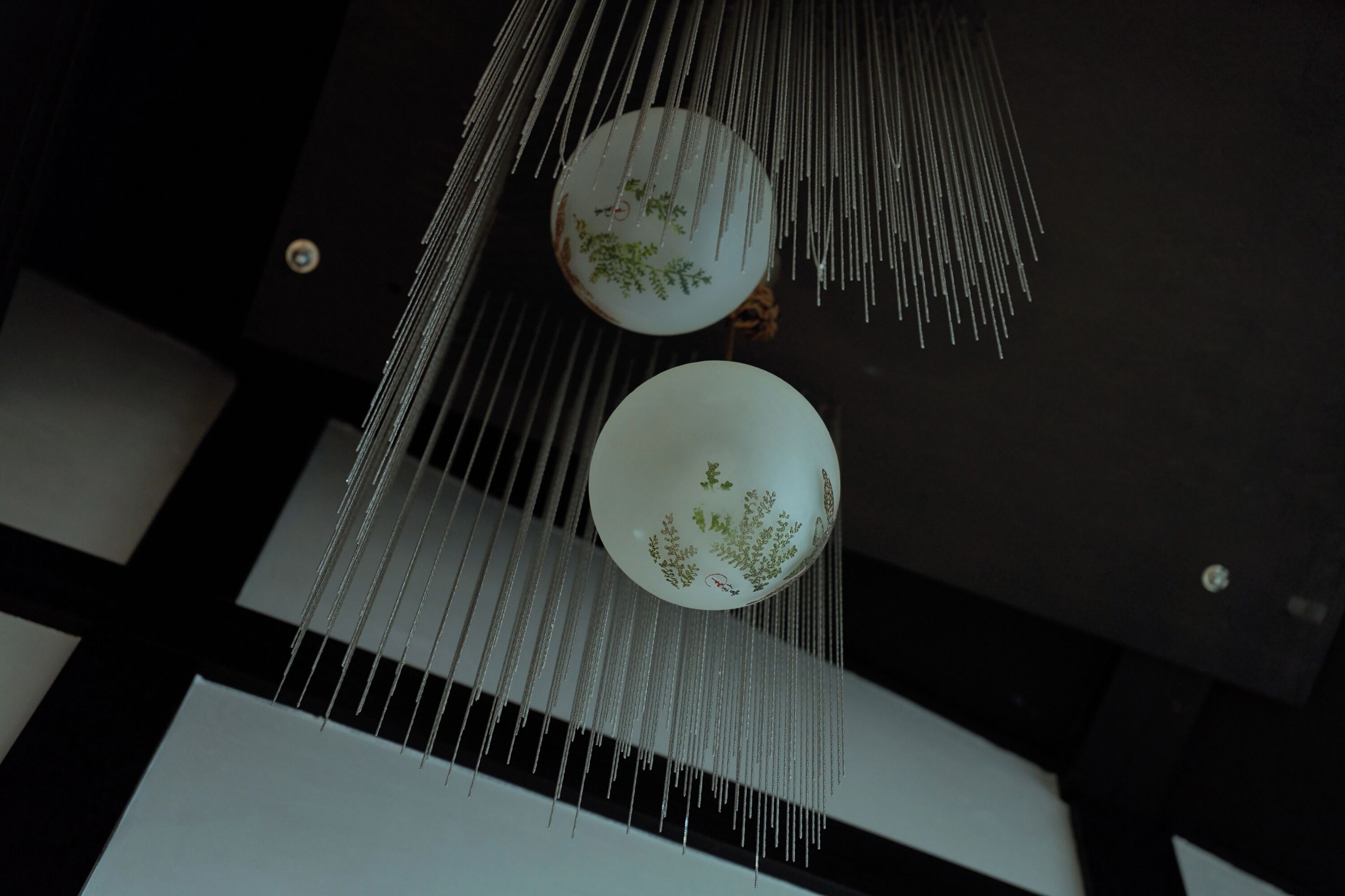 Teto com luminária pendente singular, com dois elementos esféricos e design floral.