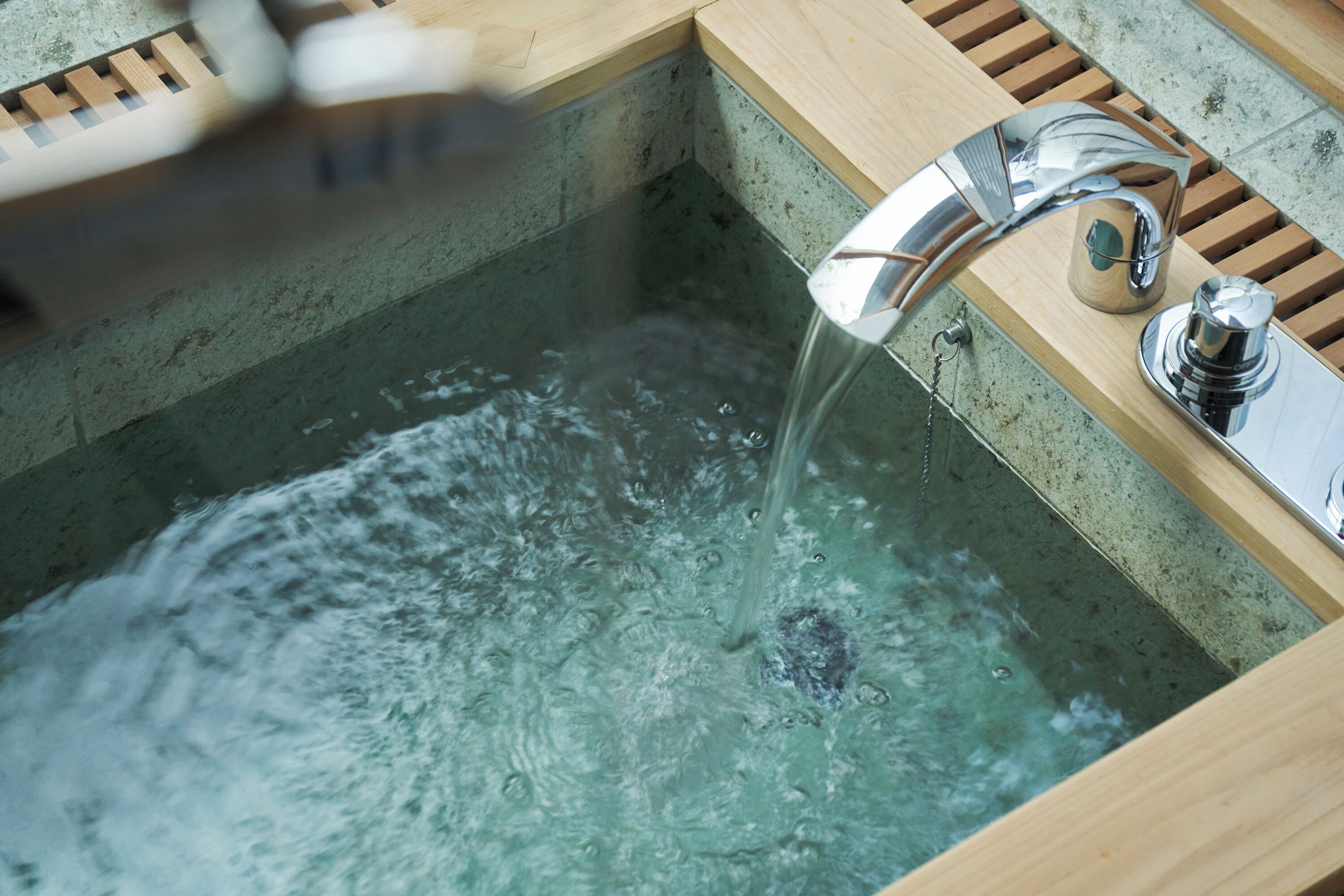 Een moderne badkamer met een houten wastafelmeubel, een chromen kraan en een bad vol water.