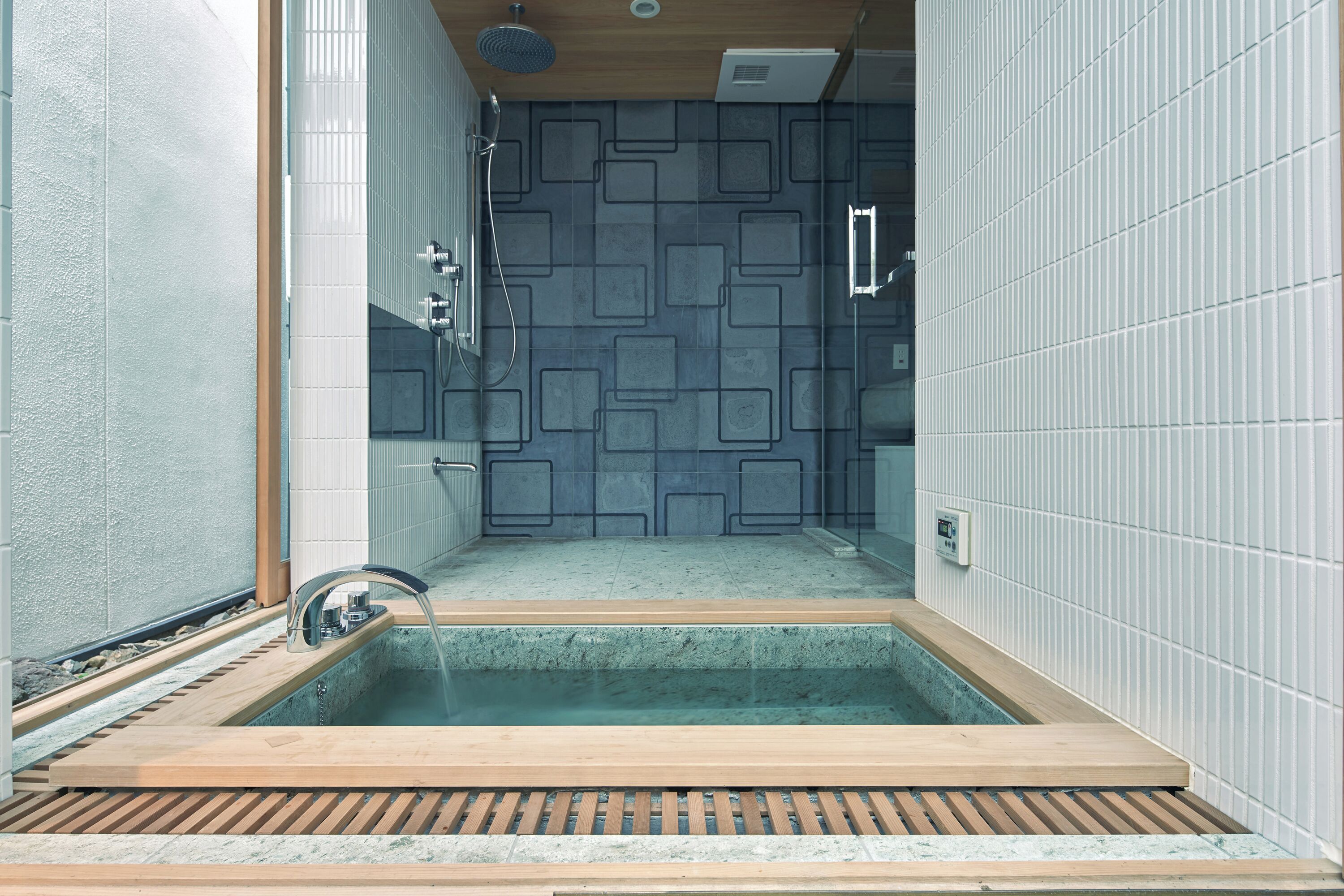 A modern bathroom with a freestanding bathtub, a shower area, and a patterned wall.