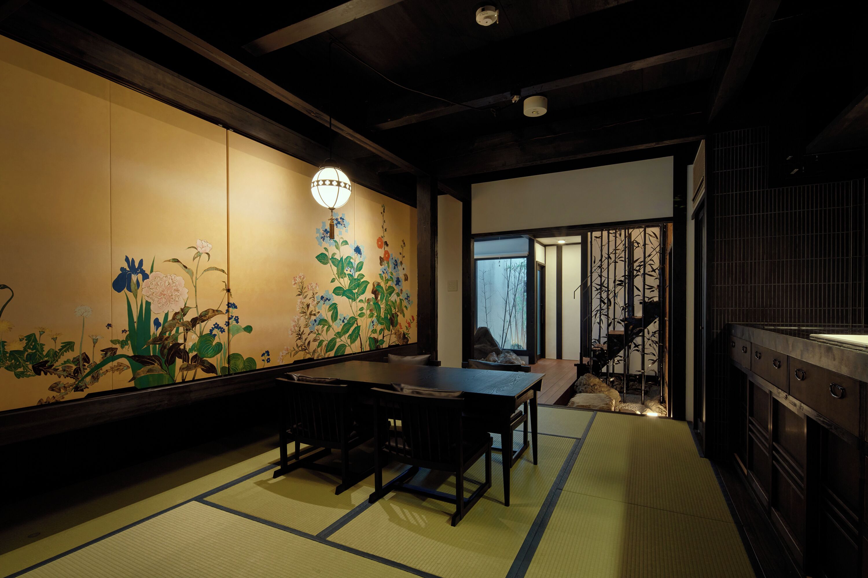 A traditional Japanese room with tatami flooring, a low table, and a wall with floral artwork.