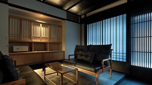 Ett traditionellt japanskt rum med tatamimattor på golvet, en svart lädersoffa, ett glasbord och skjutbara shojipaneler.