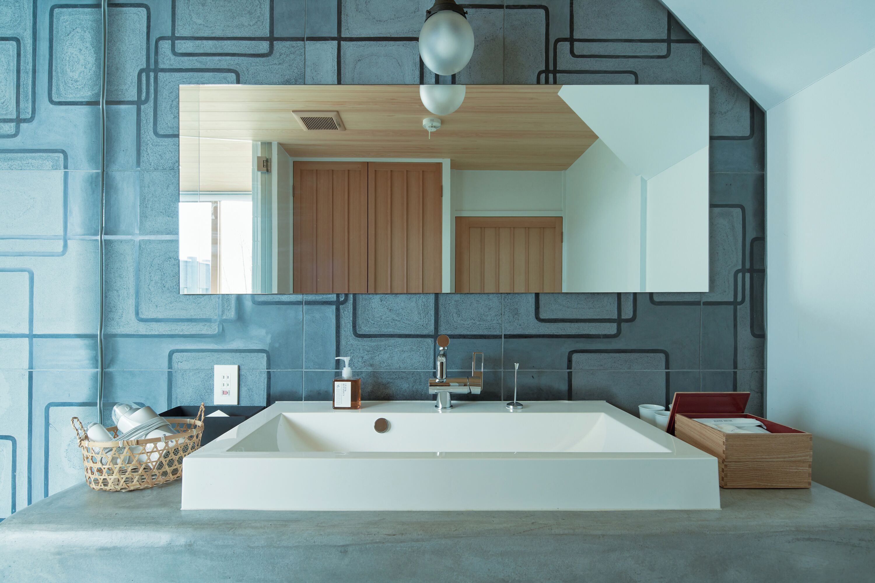 A modern bathroom with a large mirror, a white sink, and a wooden vanity.