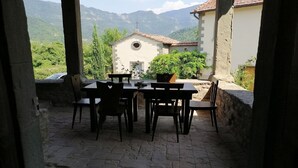 Eine Terrasse im Freien mit Steinboden, einem Tisch und Stühlen sowie Blick auf eine Berglandschaft.
