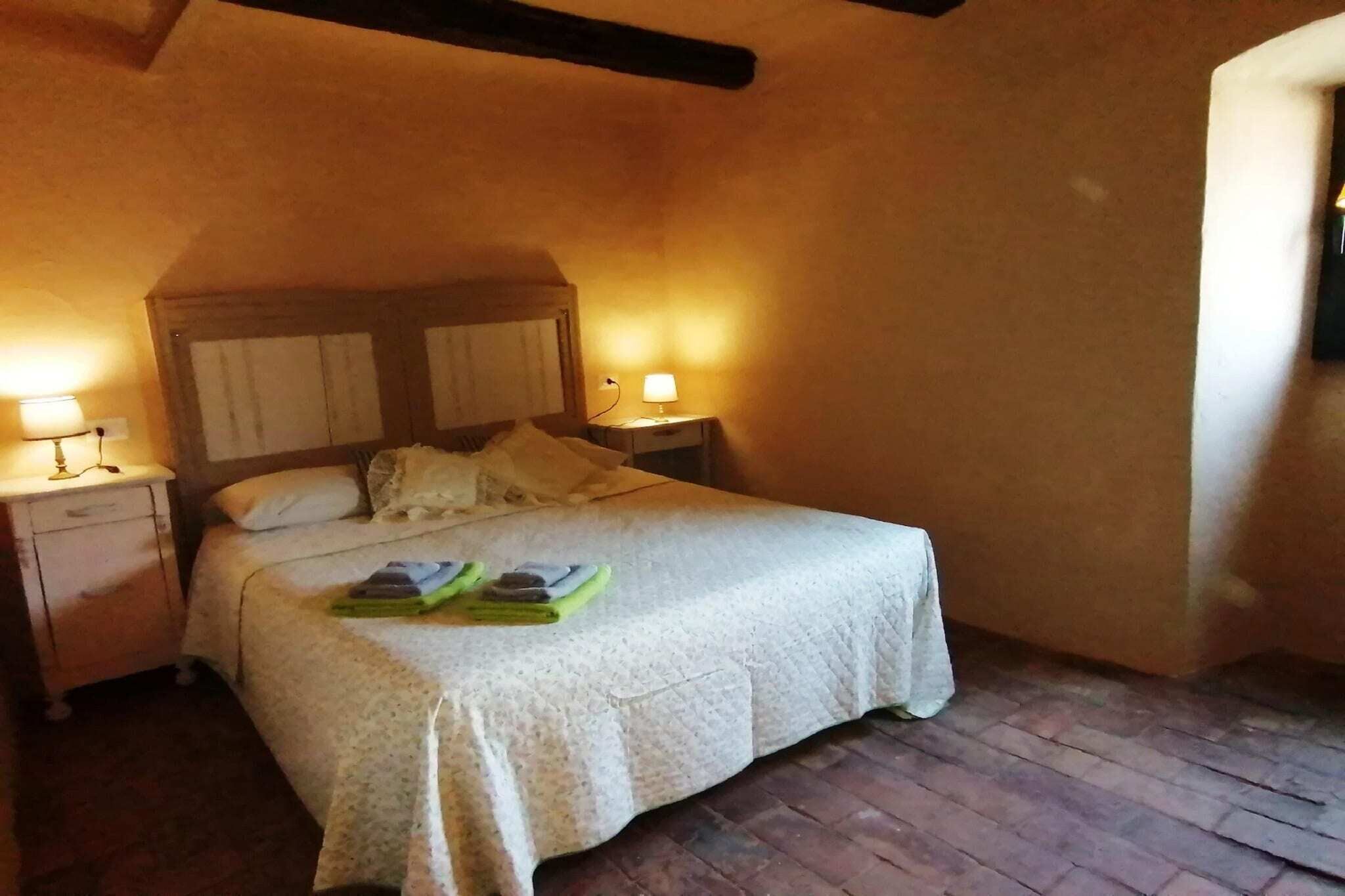 A cozy bedroom with a bed, two bedside tables with lamps, and a brick floor.