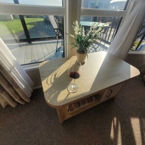 A room with a large window, a wooden table with a glass of red wine, a potted plant, and a view of a deck and outdoor area. - Beachside Lodge - Sleeps 6 - Pets ok - Plus Parking (Morecambe)