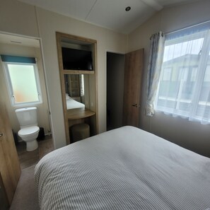 A bedroom with a bed, a wooden wardrobe, a television, a toilet, and a window with curtains. - Beachside Lodge - Sleeps 6 - Pets ok - Plus Parking (Morecambe)