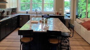 Una cocina moderna con una isla grande, armarios oscuros y vistas al exterior.