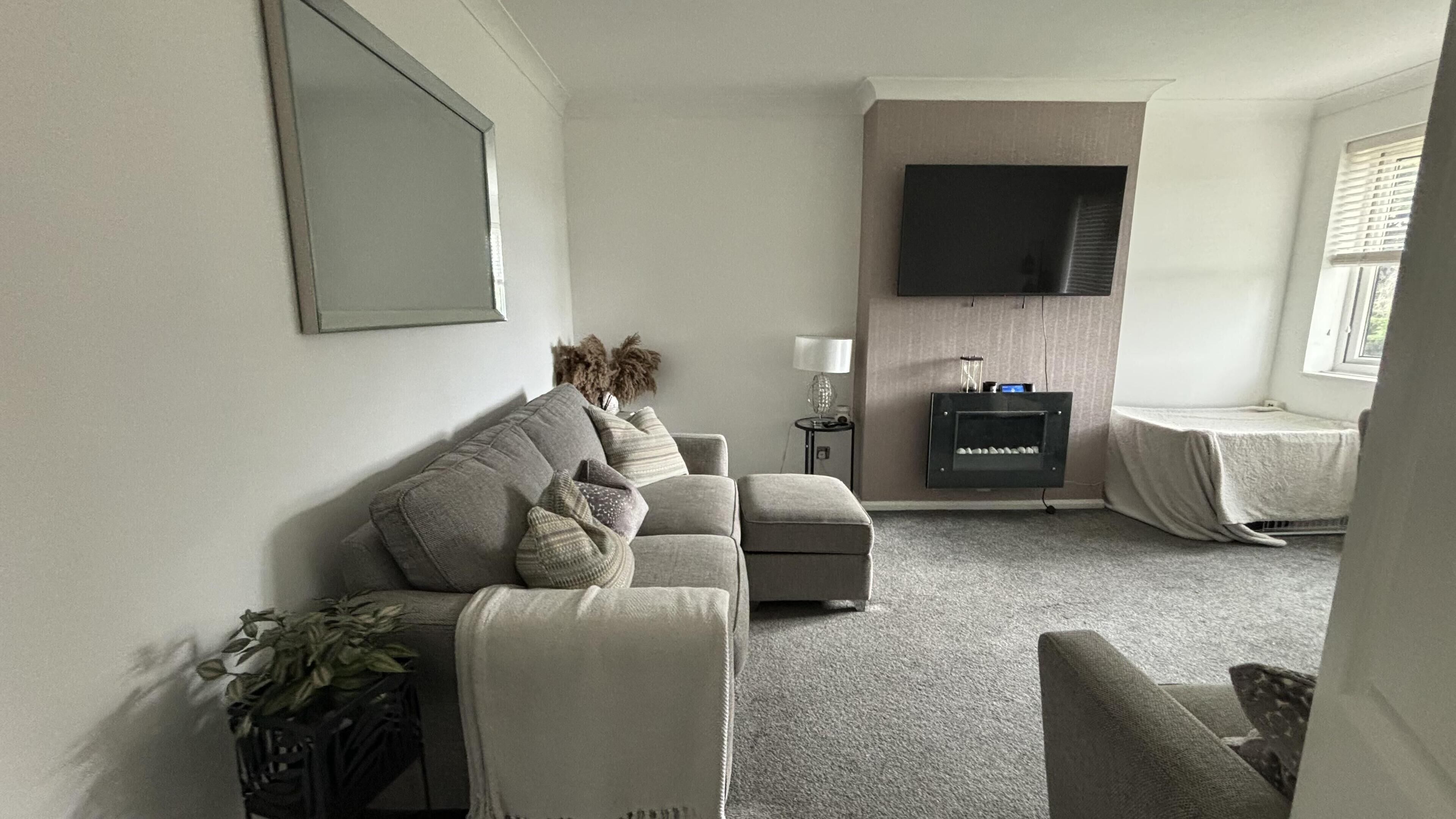 Un salon comprenant un canapé, un fauteuil et un téléviseur à écran plat fixé au mur.