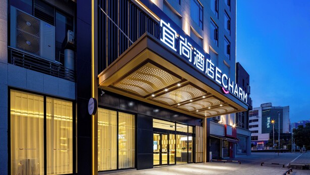 Een hotel ingang met een modern ontwerp, met een groot verlicht bord, een overdekt inkomgedeelte en grote ramen.