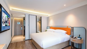 Een hotelkamer met een groot bed, een nachtkastje met telefoon en boek, een spiegel en een televisie aan de muur.