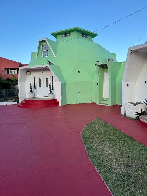 Un edificio verde con techo rojo, puerta blanca y un pequeño porche con escalones.