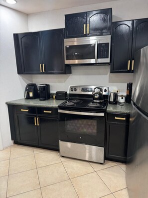 A kitchen with black cabinets, a stainless steel stove, a microwave, and a refrigerator.