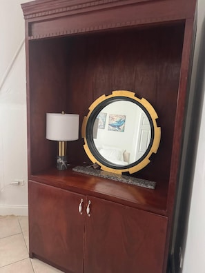 A wooden wardrobe with a mirror, a lamp, and a small shelf.