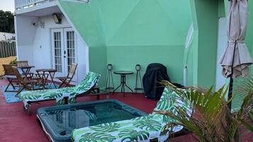 A green building with a balcony, a pool area with lounge chairs, and a covered patio.