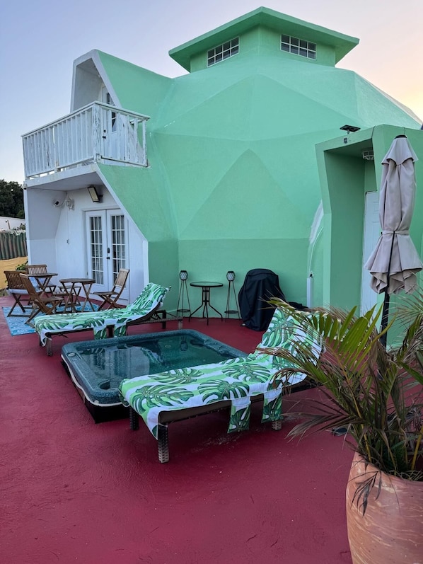 A green building with a balcony, a pool area with lounge chairs, and a covered patio.