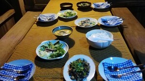 Une table à manger dressée avec différents plats et bols, entourée de murs en bois et de tableaux encadrés.