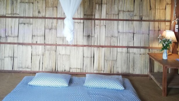 Une chambre avec un lit, une moustiquaire, un mur en bois et une table de chevet avec une lampe.