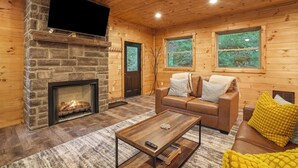 A cozy cabin interior with a stone fireplace, wooden walls, a leather sofa, and a flat-screen TV mounted above the fireplace. - Modern Rustic Retreat ~Newly Built with Hot Tub and EV charger, ~6mi to Ash Cave (Creola)