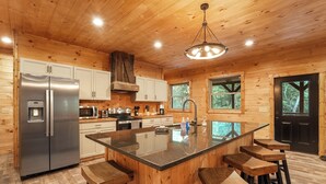 A wooden cabin interior with a large kitchen island, stainless steel refrigerator, and wooden bar stools. - Modern Rustic Retreat ~Newly Built with Hot Tub and EV charger, ~6mi to Ash Cave (Creola)