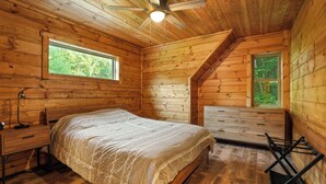 A wooden cabin bedroom with a bed, dresser, and a window overlooking greenery. - Modern Rustic Retreat ~Newly Built with Hot Tub and EV charger, ~6mi to Ash Cave (Creola)