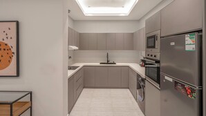 A modern kitchen with grey cabinets, a central island, a built-in oven, and a refrigerator with a fresh produce sticker. - Mabaat - Al Narjis - 549 (Riyadh)