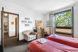 Une chambre d’hôtel avec deux lits, une chaise, une commode et une grande fenêtre donnant sur la forêt.