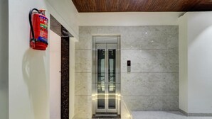A modern elevator with a marble wall and a fire extinguisher mounted on the wall. - Archit By Glitz Hotels (Navi Mumbai)