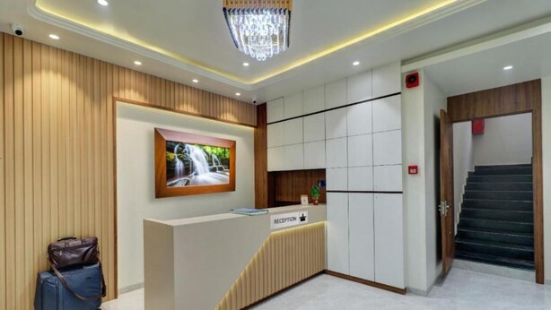 A reception area with a reception desk, a mounted television, a staircase, and a security camera. - Archit By Glitz Hotels (Navi Mumbai)