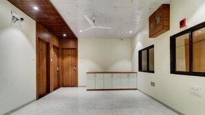 A hallway with wooden doors, a white ceiling, and a ceiling fan. - Archit By Glitz Hotels (Navi Mumbai)