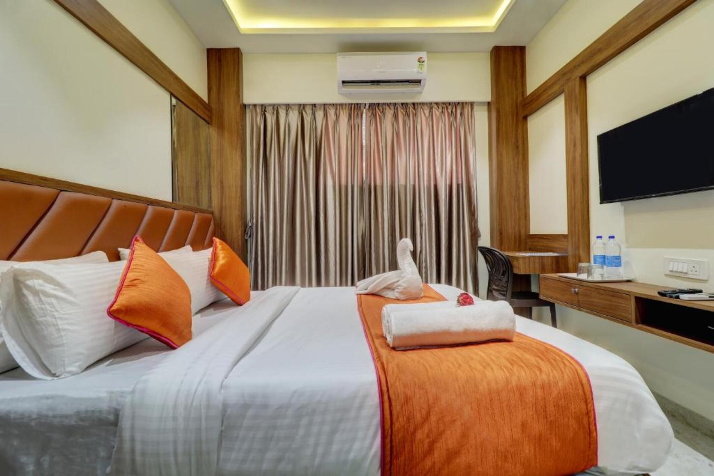 A hotel room with a bed, a desk, a chair, an air conditioning unit, and a television.