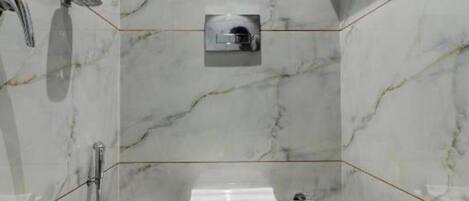 A bathroom with a marble wall, a toilet, a hand dryer, and a towel rack.