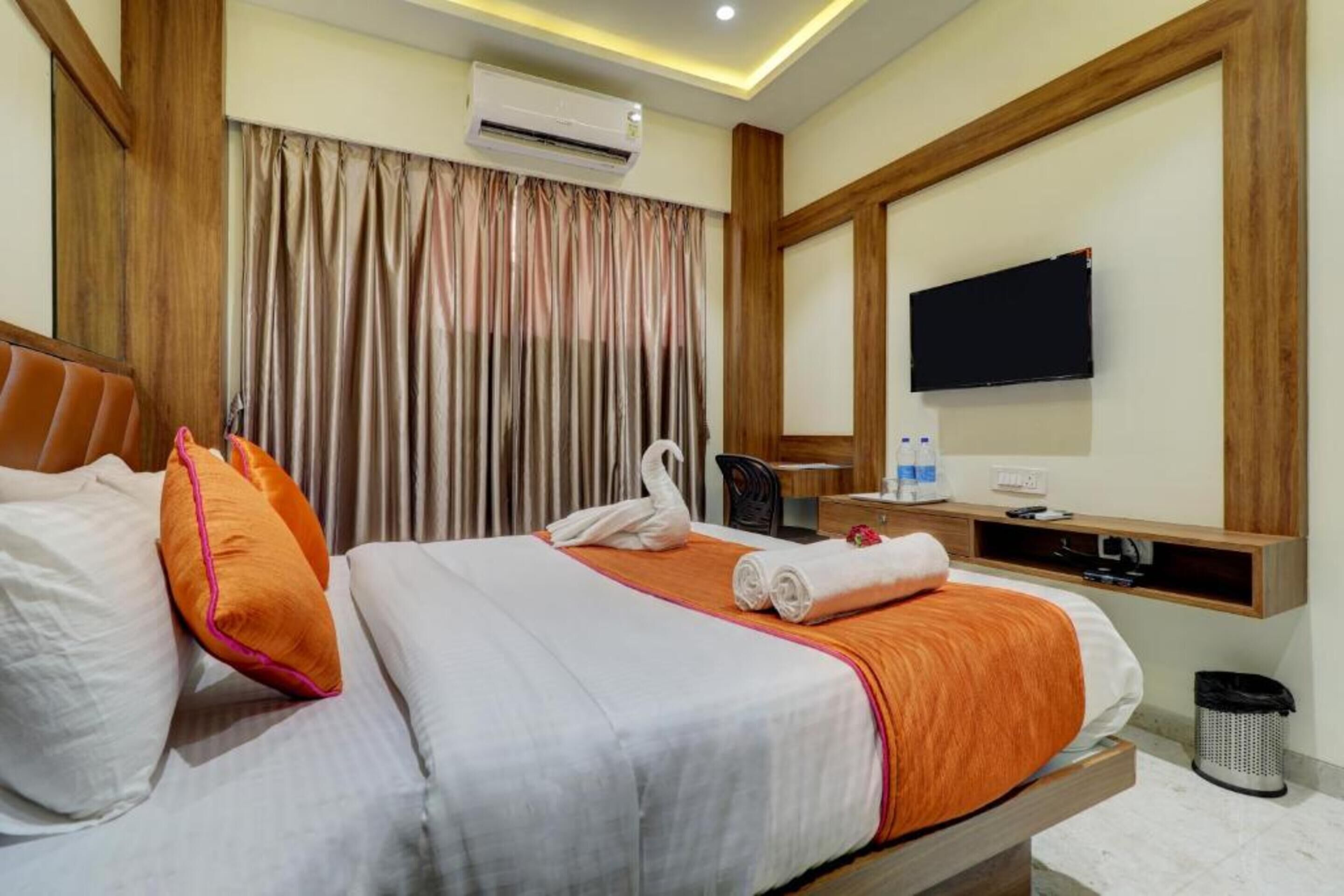 A hotel room with a bed, pillows, a TV, a desk, and a trash bin.