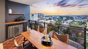 Ein Balkon mit Holztisch, Stühlen und Blick auf eine Stadtlandschaft bei Sonnenuntergang.