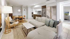 Ein modernes Wohnzimmer mit einer Couch, einem Esstisch mit Stühlen, einem Couchtisch und einer Küchenzeile mit Kühlschrank und Herd.