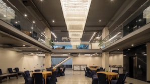 A spacious, modern conference room with high ceilings, a large chandelier, and multiple tables and chairs. - The Aldott Hotel (Gurugram)