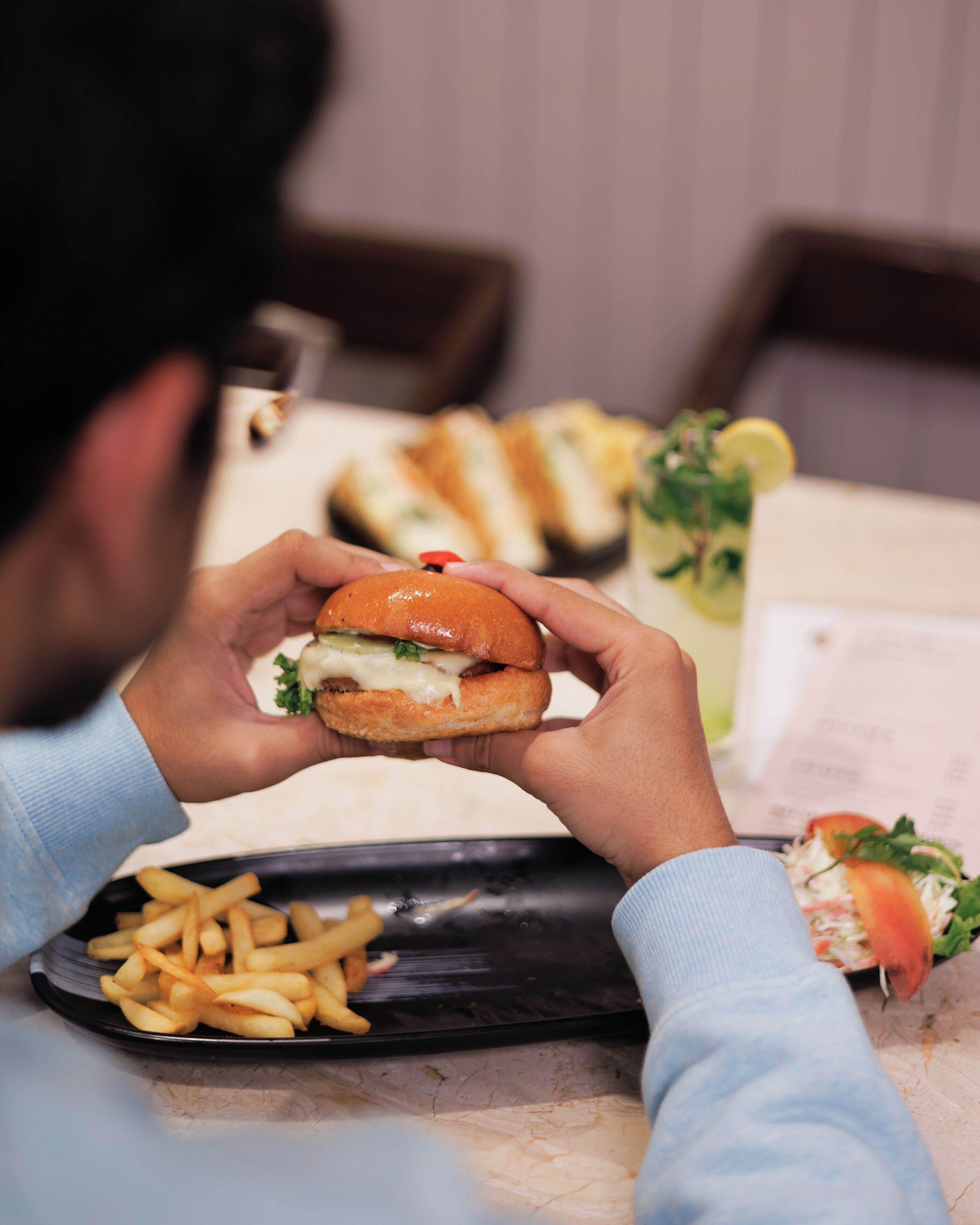 Een persoon houdt een broodje hamburger met friet op een dienblad.