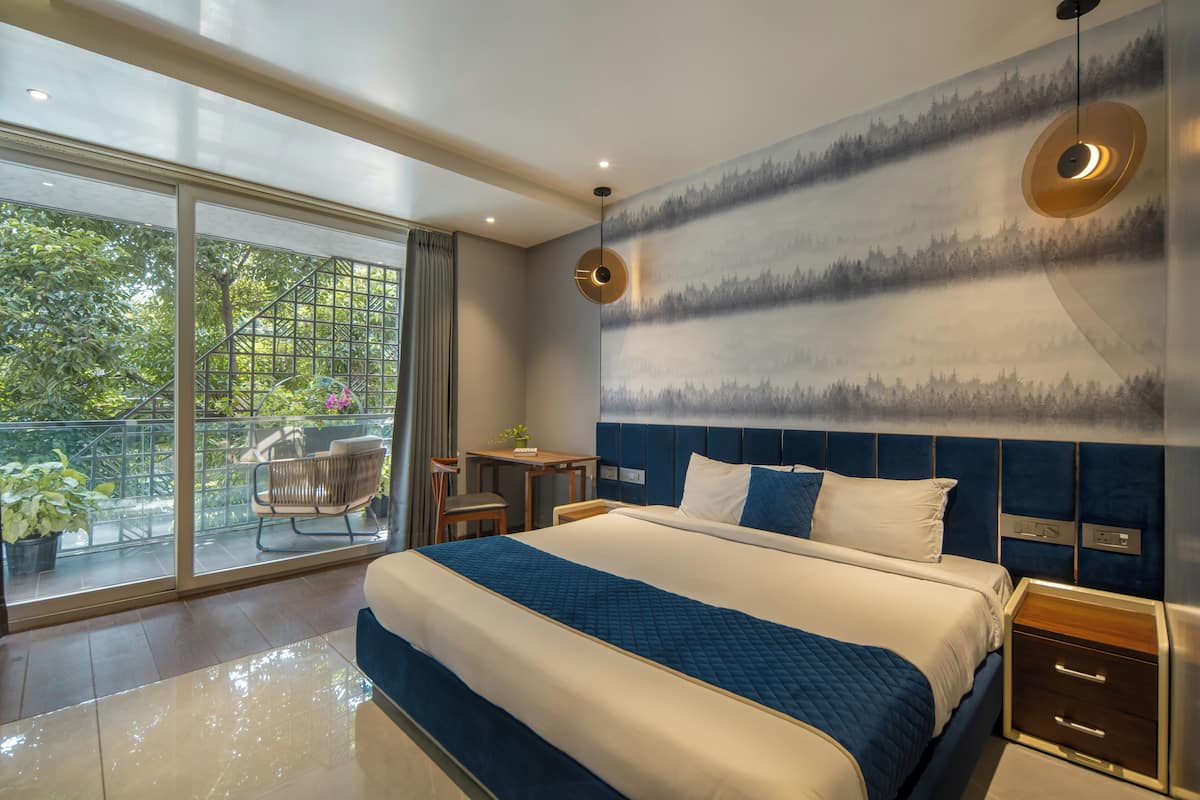 A modern hotel room with a large bed, a balcony with a view of greenery, and a wall with a forest mural.