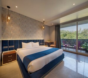 A modern bedroom with a large bed, a nightstand, a small table, and a balcony with chairs. - The Aldott Hotel (Gurugram)
