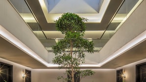 A modern atrium with a skylight, potted plants, and a central seating area. - The Aldott Hotel (Gurugram)