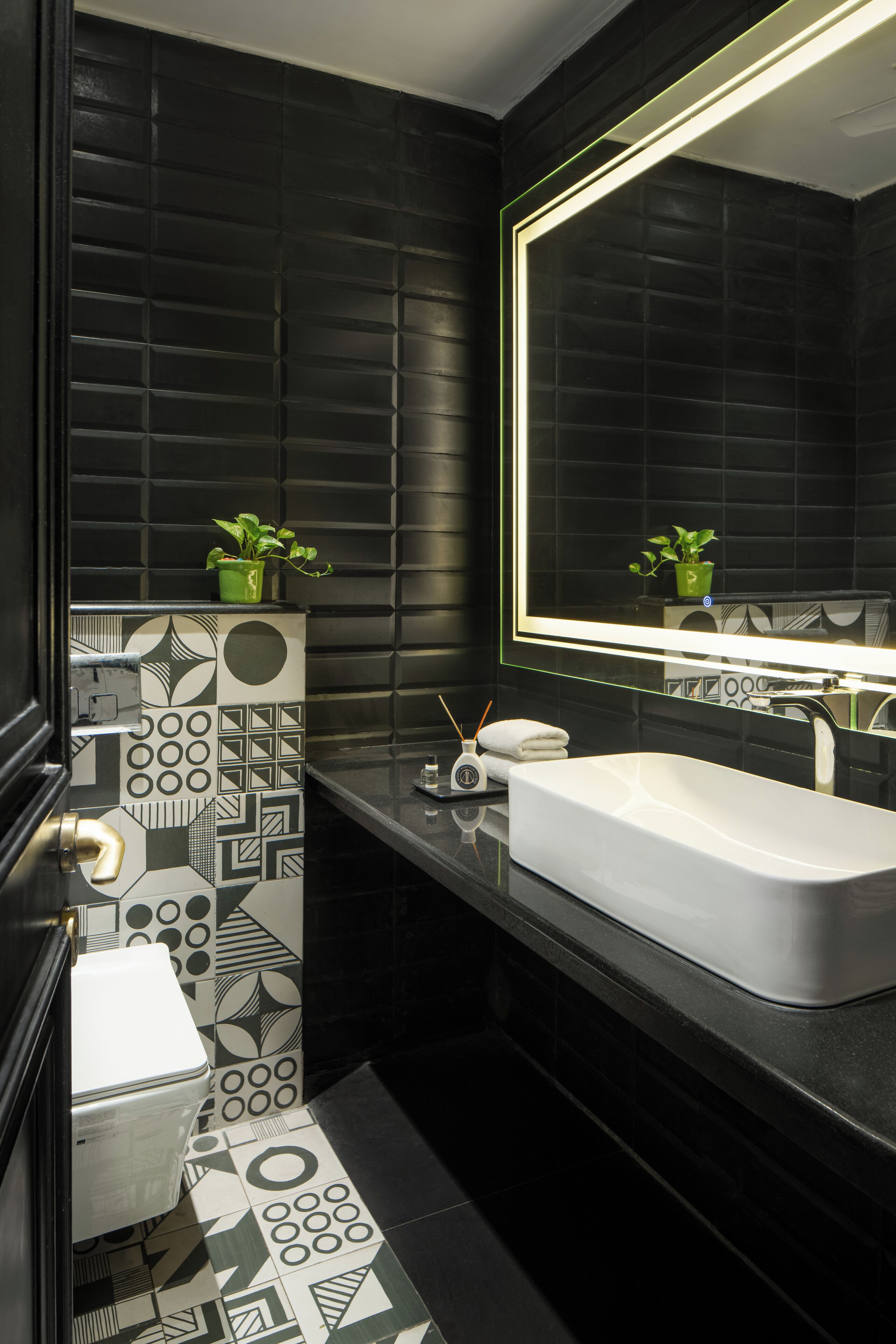 Un bagno moderno con pavimento piastrellato in bianco e nero, un lavandino bianco e uno specchio grande con una pianta verde sul ripiano.